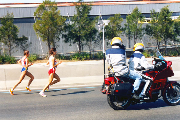 Two runners being filmed from a motorcycle